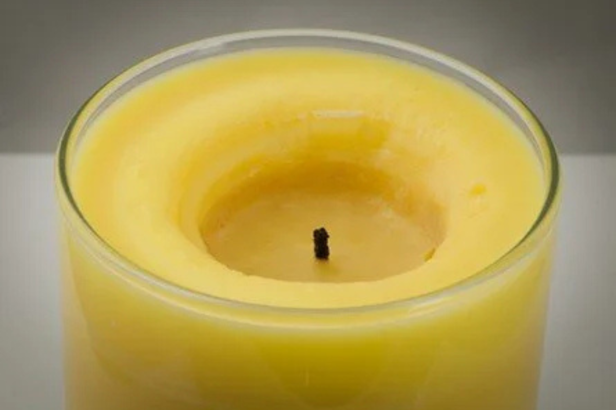Yellow candle showing wax tunneling in a glass container with a gray background
