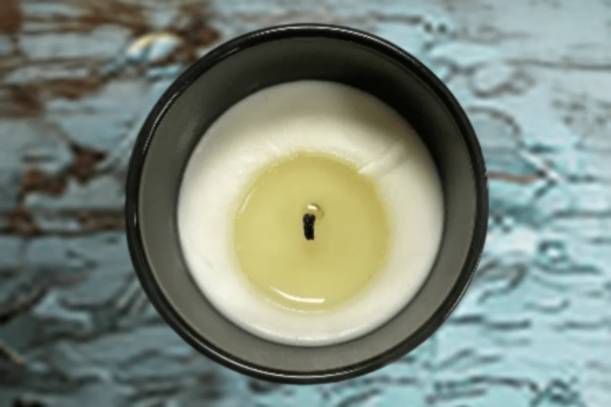 Candle showing wax tunneling in a black container with a wick on a textured surface